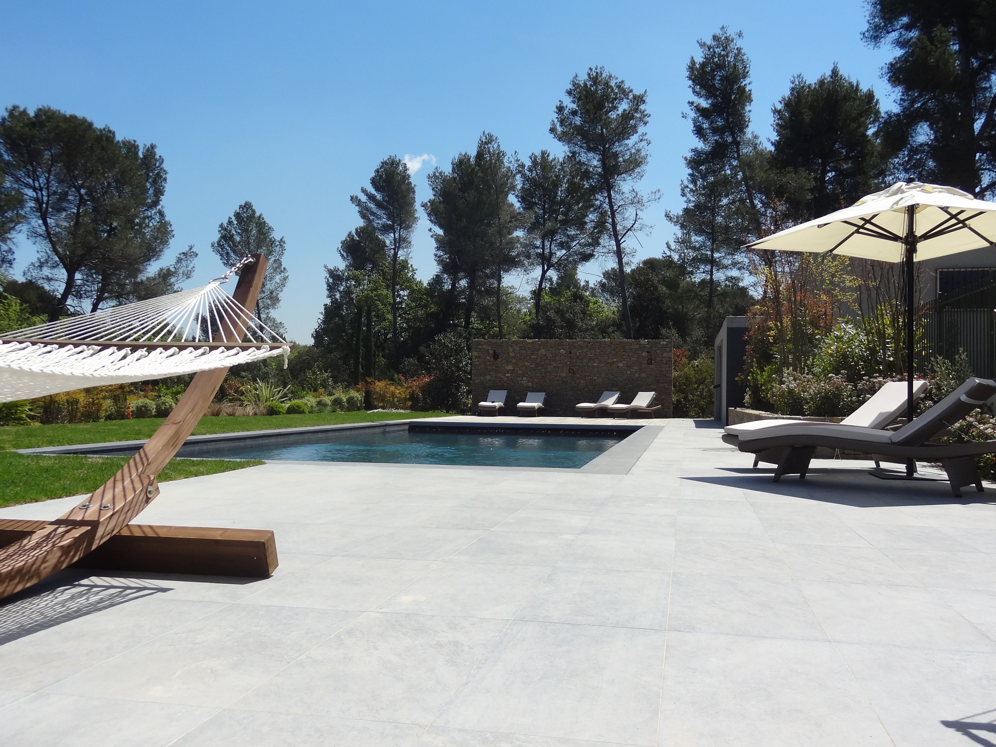 A pool area with a hammock, lounge chairs, and a stone wall.