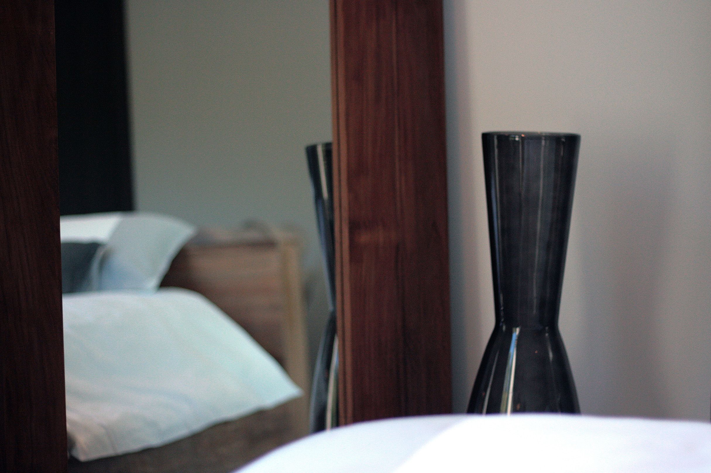 A bedroom with a bed, a wooden nightstand, and a vase on the nightstand.