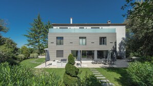 A modern two-story house with a flat roof, large windows, and a patio area with outdoor furniture. - Domaine Rampale (Fuveau)