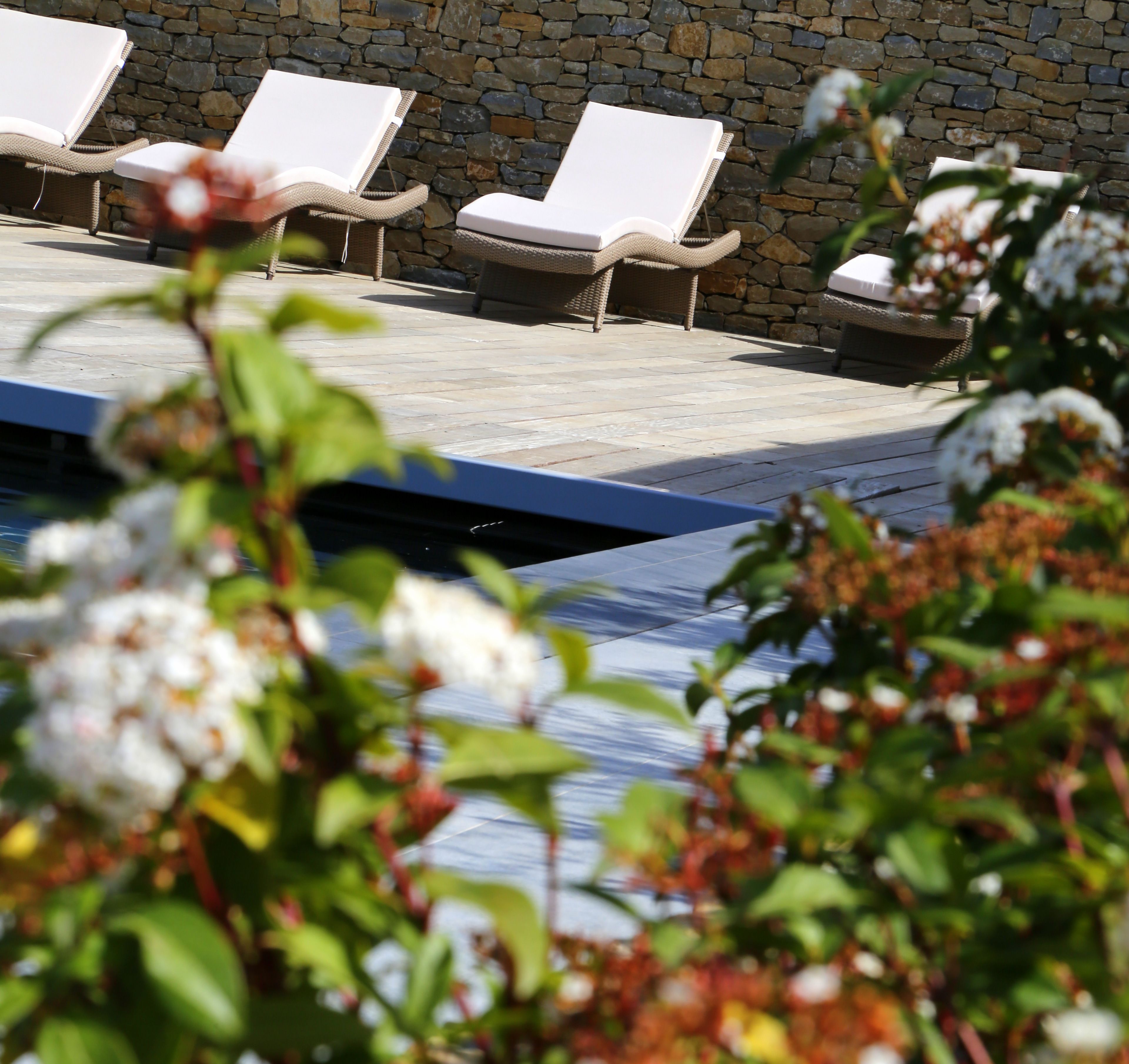 A pool area with lounge chairs and a stone wall in the background.