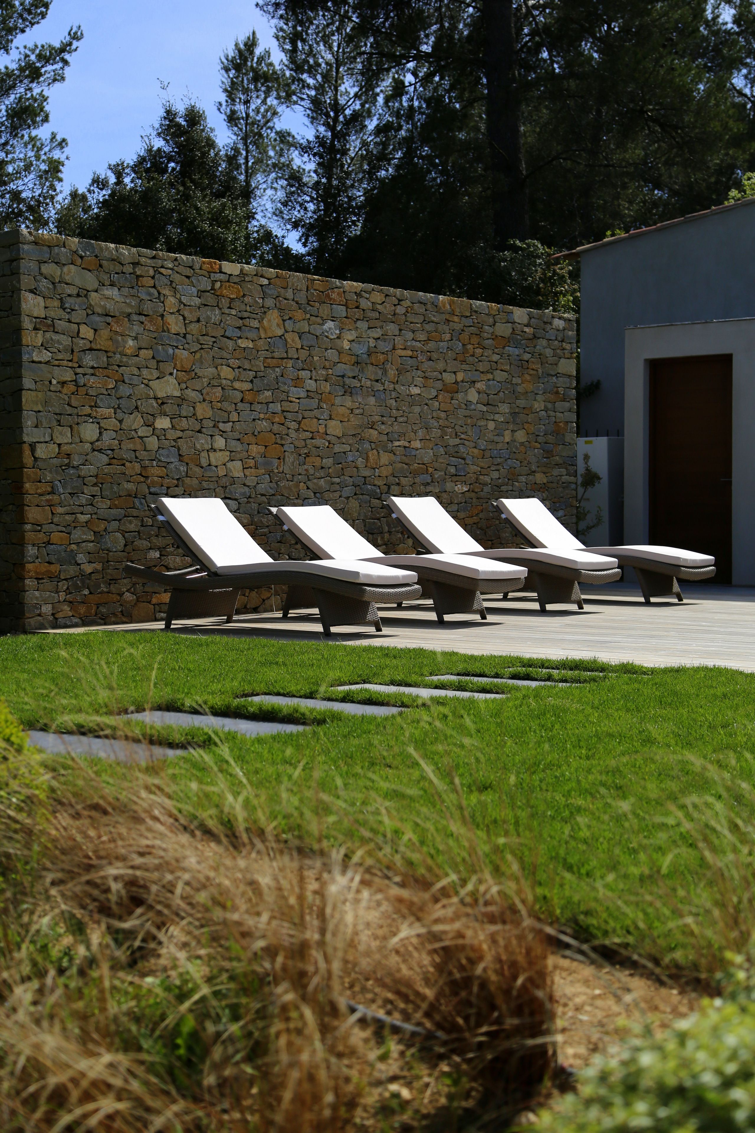 A stone wall with a row of lounge chairs aligned against it.
