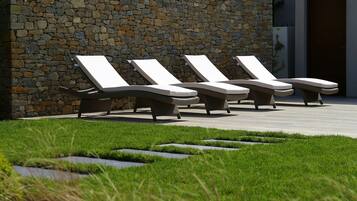 A stone wall with a row of lounge chairs aligned against it.