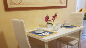 A dining table with white chairs, a vase with pink flowers, and a framed map on the wall. - B&B Girasole (Rome)