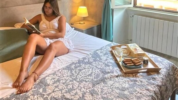 A person sitting on a bed in a room with a window, a lamp, and a tray with food items. - B&B Girasole (Rome)