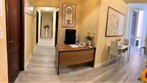 A hallway with a desk, a chair, and a dining table with chairs. There are two vases with flowers on the dining table. - B&B Girasole (Rome)