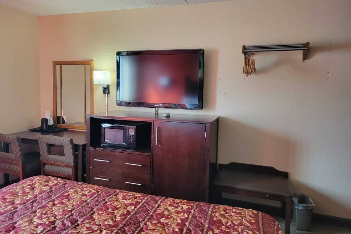 A hotel room with a bed, a TV, a desk, a mirror, and a trash bin.