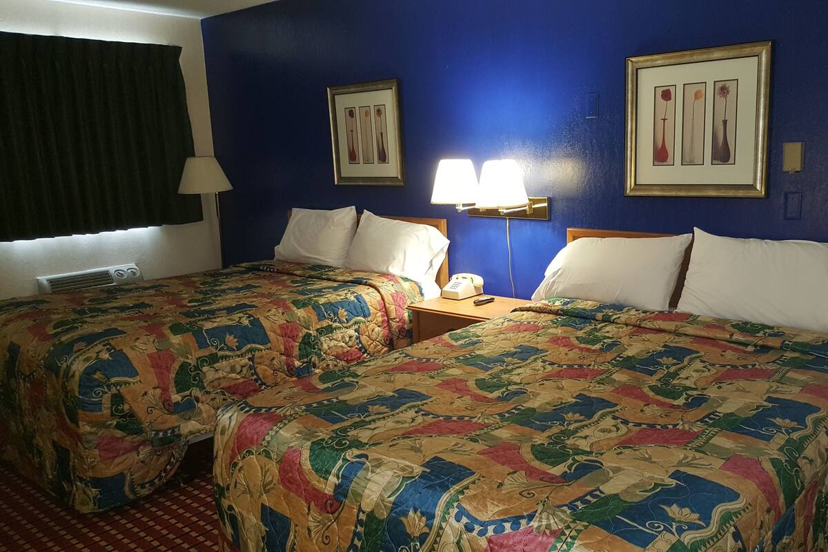 A hotel room with two beds, a nightstand with a lamp, and two framed pictures on the wall.