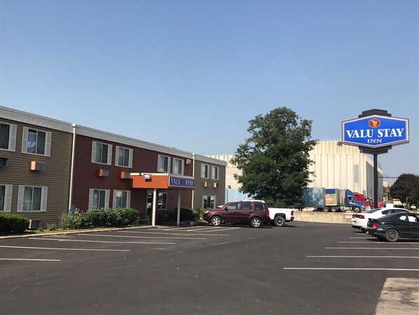 A parking lot with a Valu Stay Inn sign, a building with multiple windows, and a large tree.