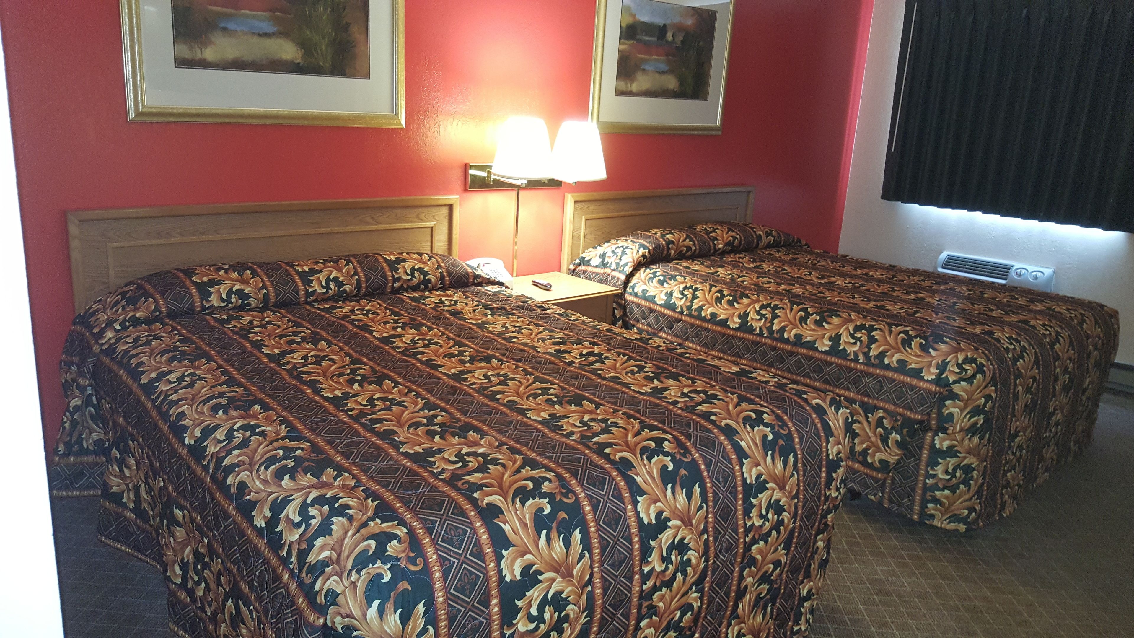 A hotel room with two beds, a nightstand, a lamp, and two framed pictures on the wall.