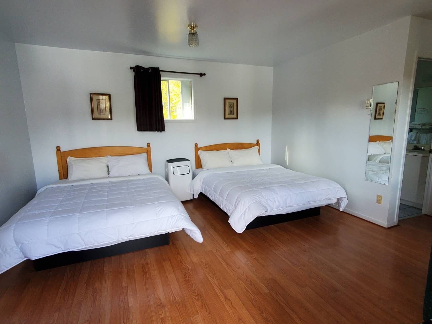 A room with two single beds, a small heater, a window with curtains, and a mirror on the wall.