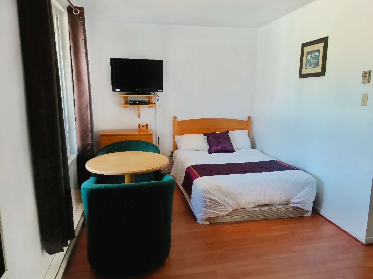 A small, neatly arranged bedroom with a bed, a TV mounted on the wall, a small table, and a chair.