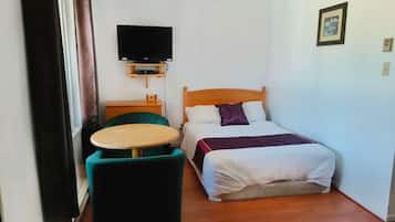 A small, neatly arranged bedroom with a bed, a TV mounted on the wall, a small table, and a chair.
