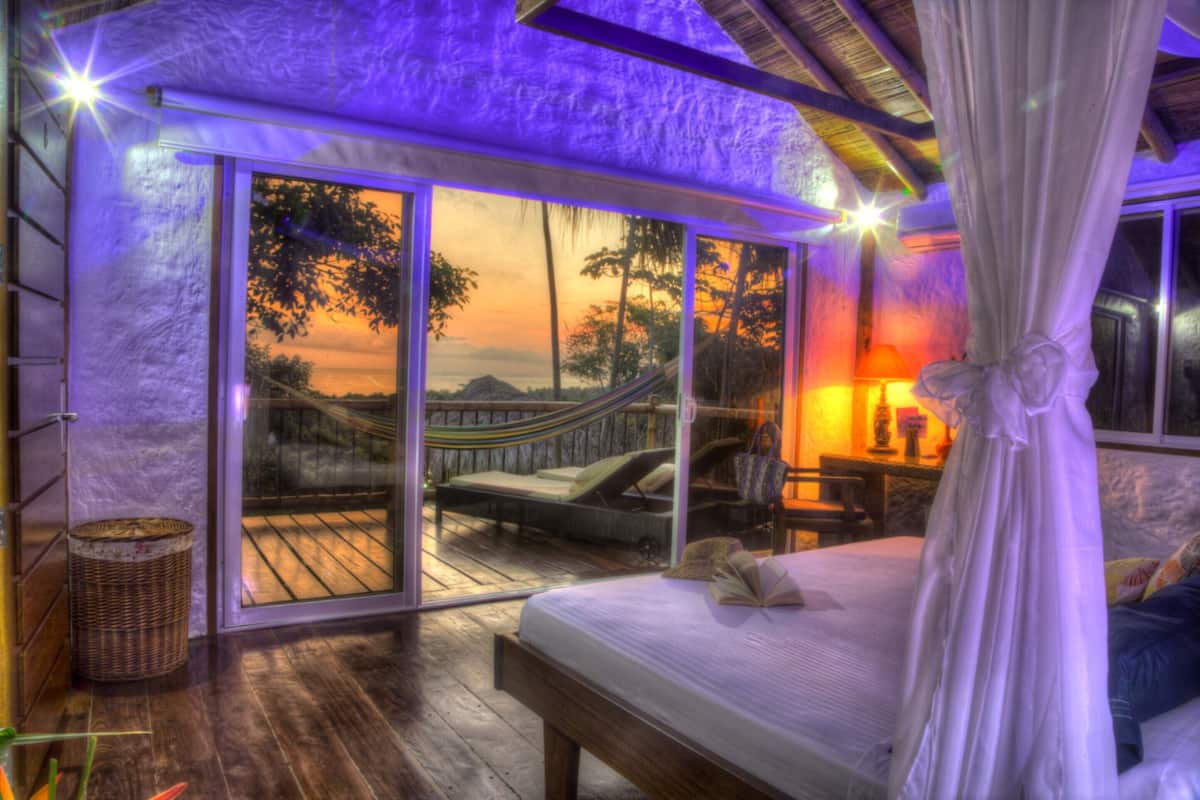 Un dormitorio con una cama, una hamaca y vistas al atardecer a través de puertas correderas grandes.