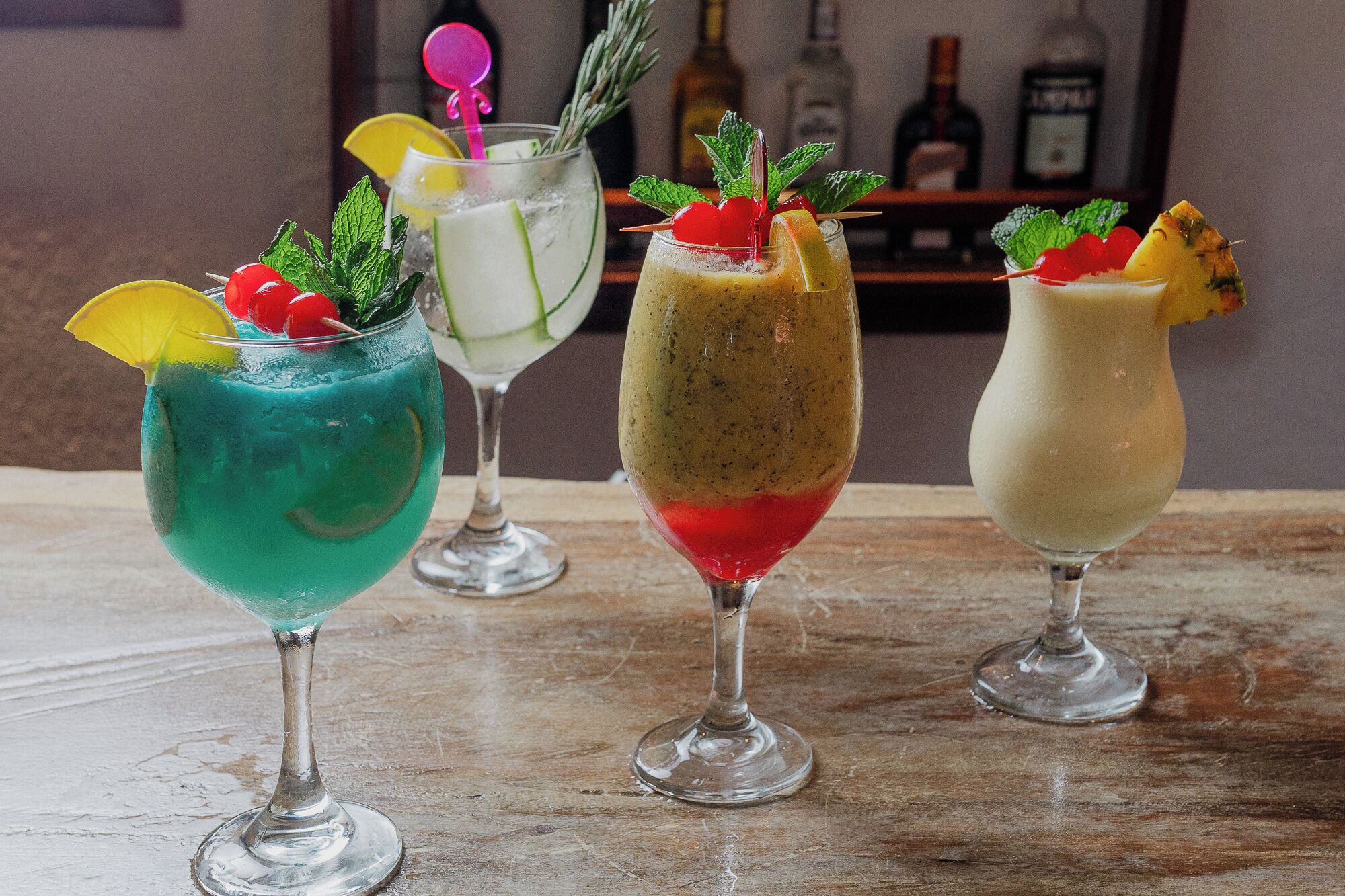 Three cocktails in different glasses on a wooden surface.
