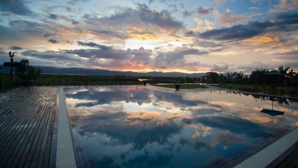A reflective pool at sunset with a wooden deck and distant mountains.