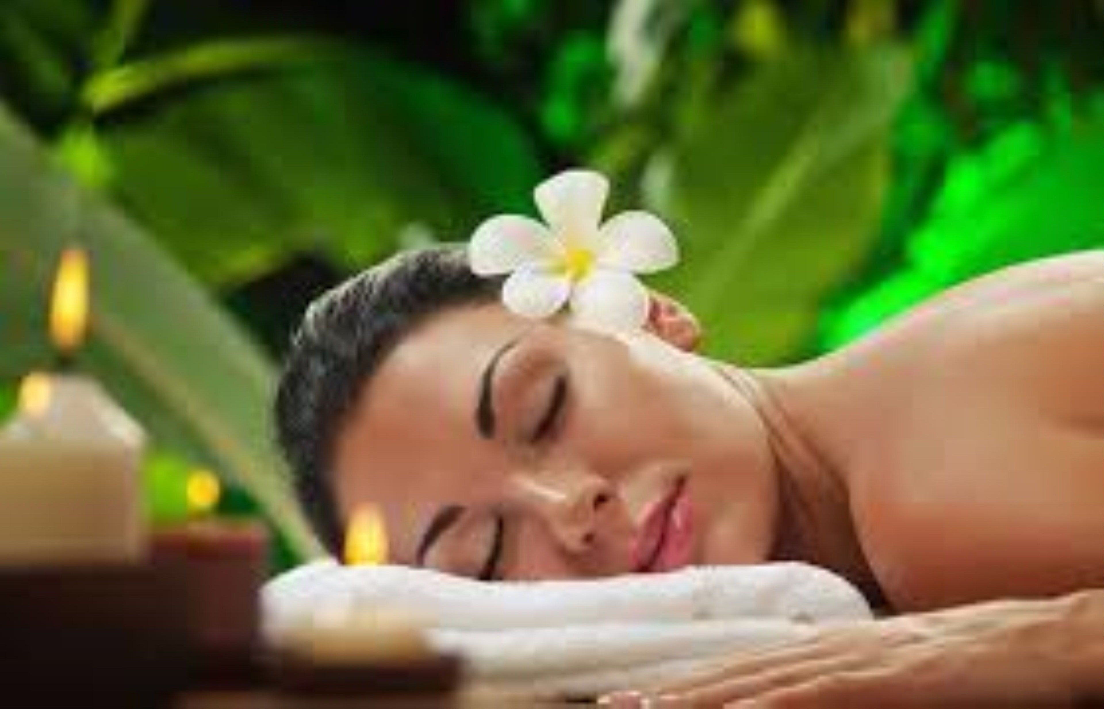 A person lying down with a flower on their head, surrounded by greenery.
