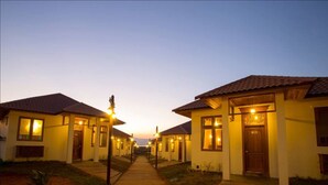 A row of single-story buildings with a central pathway, each with a door and windows, under a clear sky.