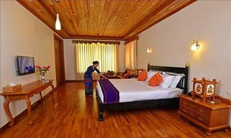 Habitación de hotel con techo de madera, una cama con almohadas naranjas, un aparador de madera y un escritorio con un jarrón de flores.