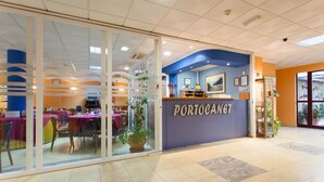 Un restaurante con entrada de vidrio, una decoración en tonos azul y naranja, y un letrero que dice 'PORTOCANET'.