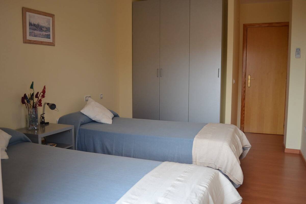 A hotel room with two beds, a wardrobe, a desk with a lamp, and a framed picture on the wall.