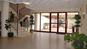 Un interior espacioso con una escalera, plantas en macetas y vistas al exterior.