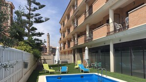 Una piscina con sillones de descanso, un patio cubierto y vista a una torre alta al fondo.