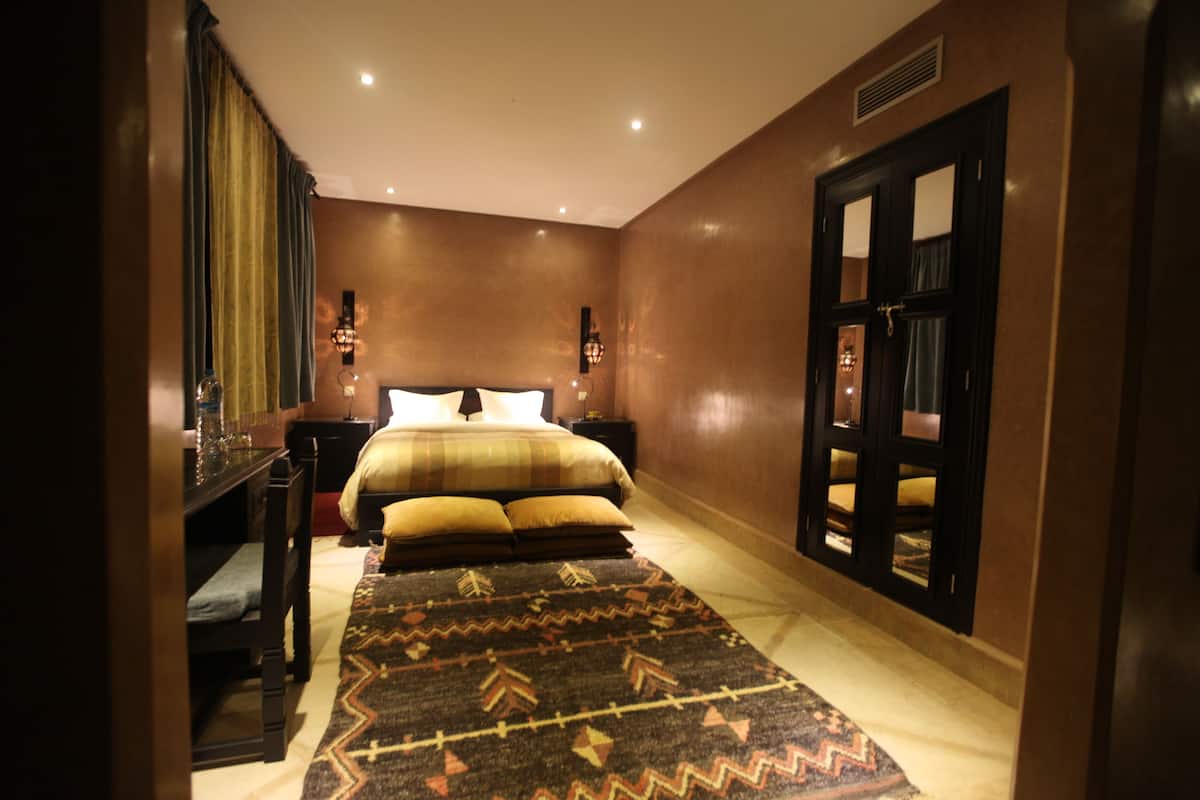 A hotel room with a bed, bedside tables, a nightstand, a rug, and a door with a mirror.