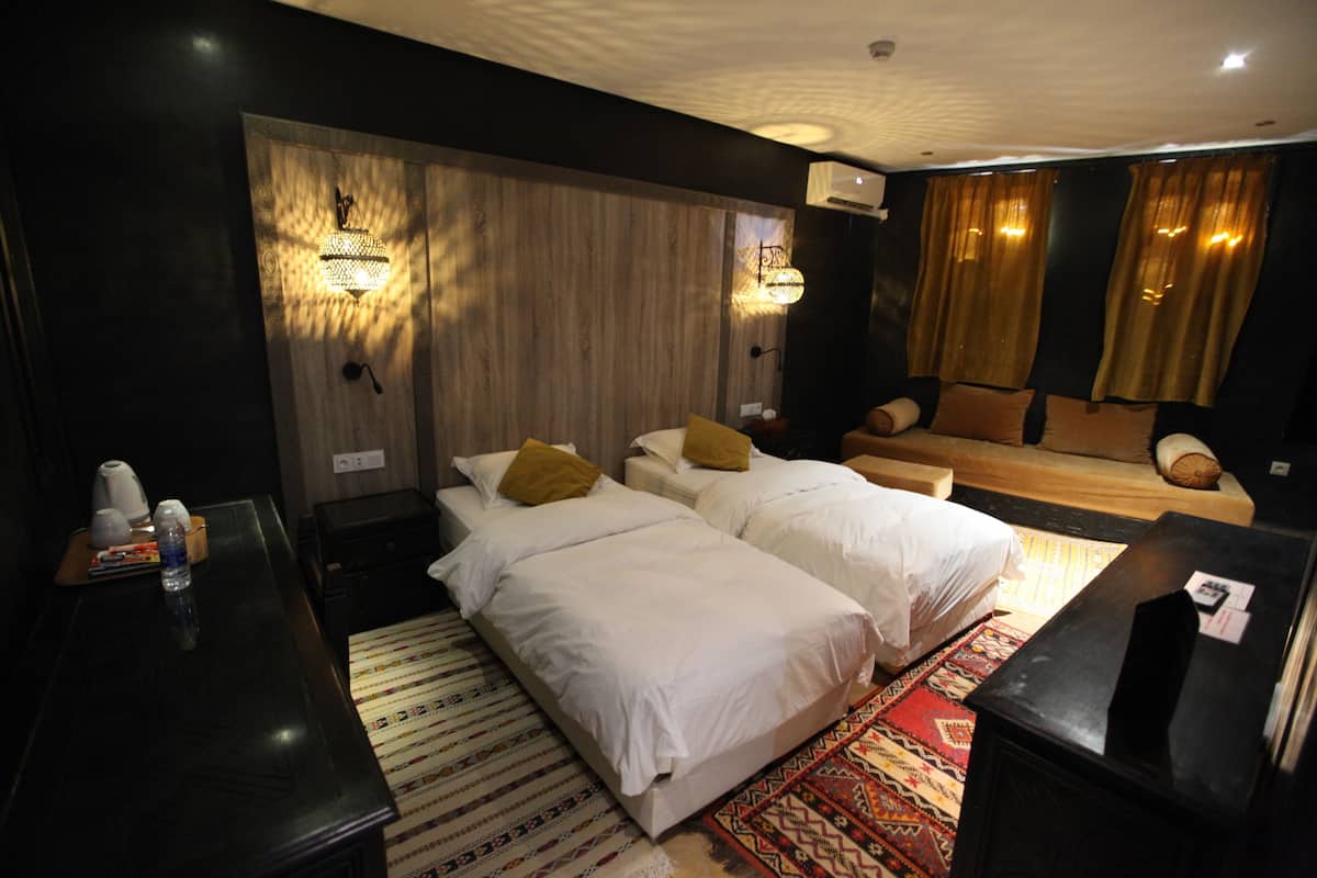 A hotel room with two beds, a desk, a chair, a small table, and a sofa.