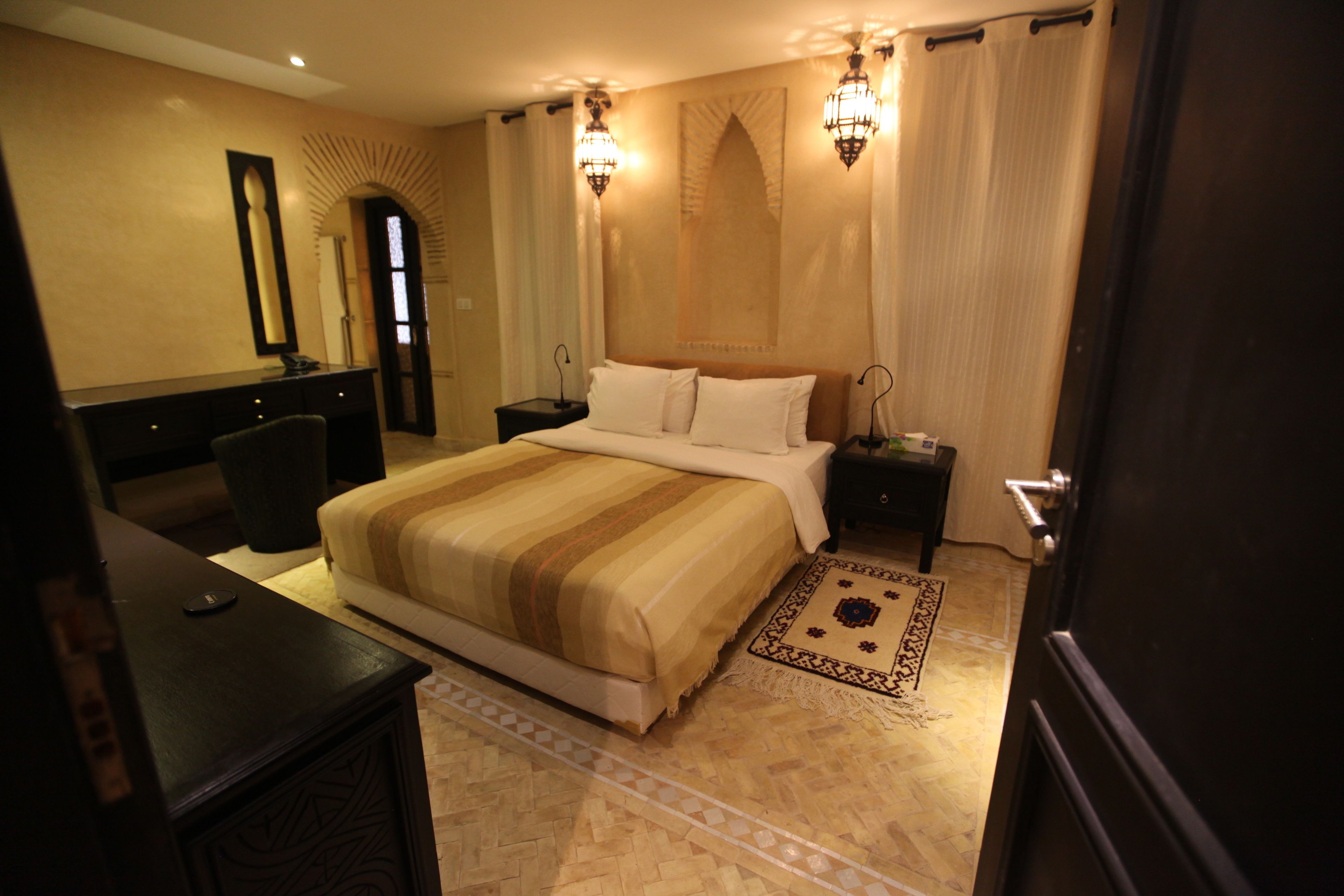 Habitación de hotel con una cama grande, dos mesitas de noche, un escritorio, un espejo y dos lámparas de pared.