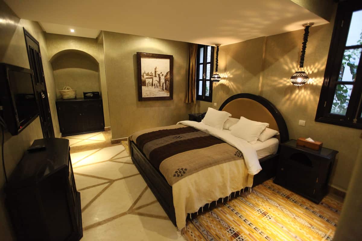 A bedroom with a large bed, a television, a desk, and a window with curtains.