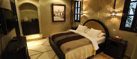 A bedroom with a large bed, a television, a desk, and a window with curtains.