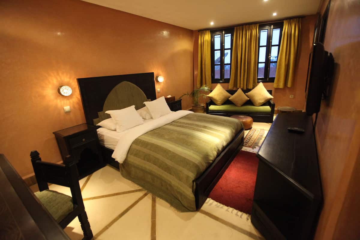 A hotel room with a large bed, a sofa, a TV, and a desk.