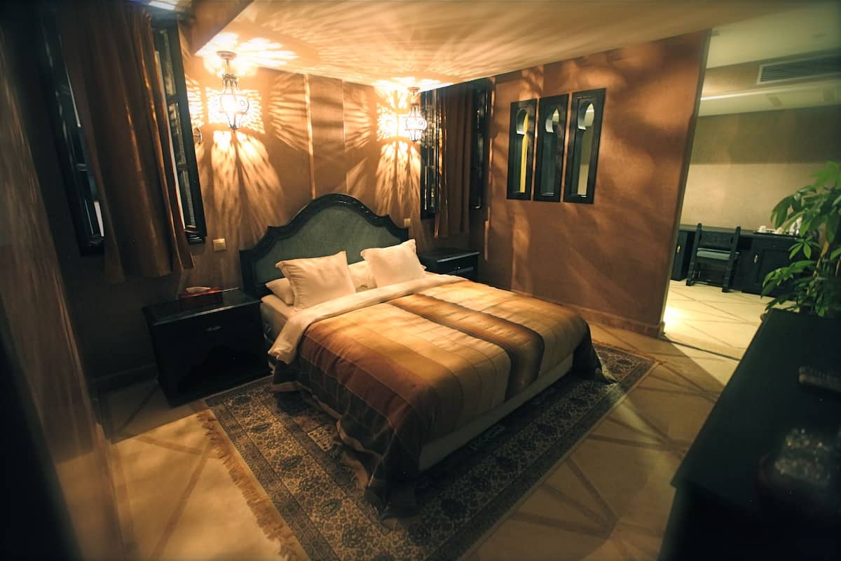 A bedroom with a large bed, nightstands, a mirror, and a chandelier.