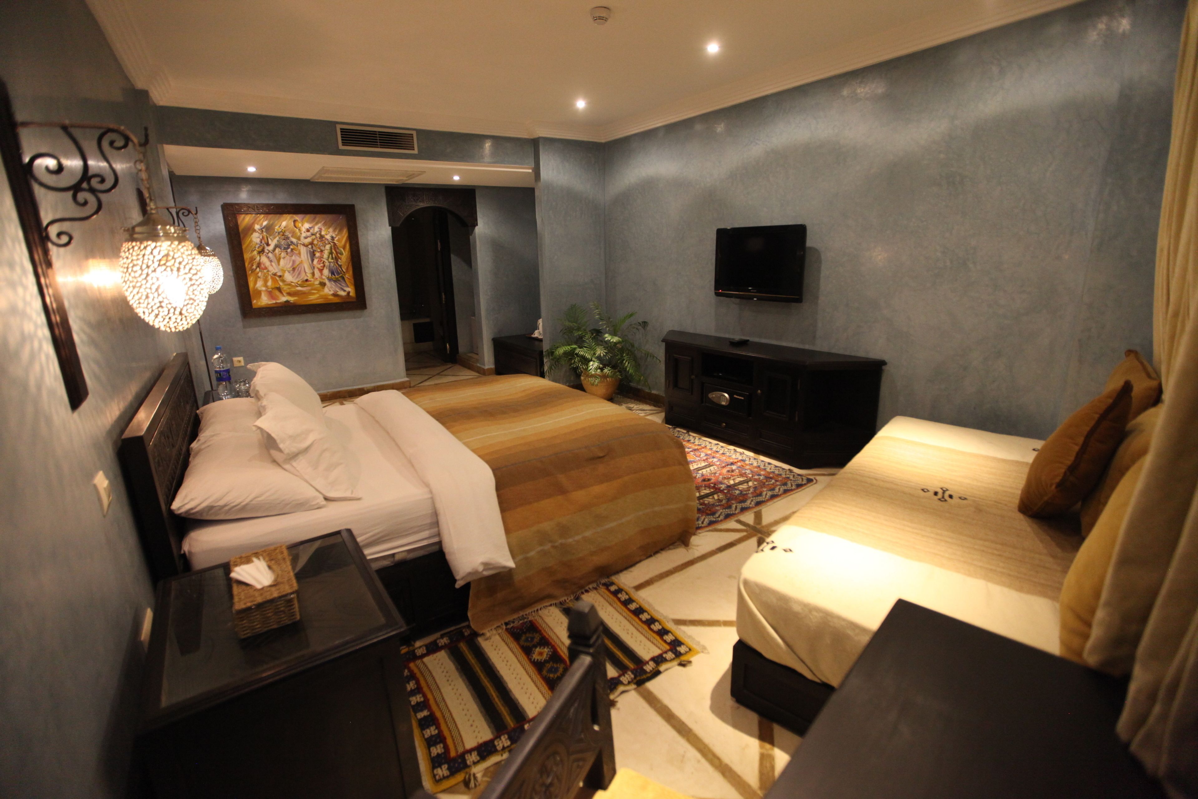 A modern hotel room with a large bed, a flat-screen TV, a bedside table, and a decorative wall piece.