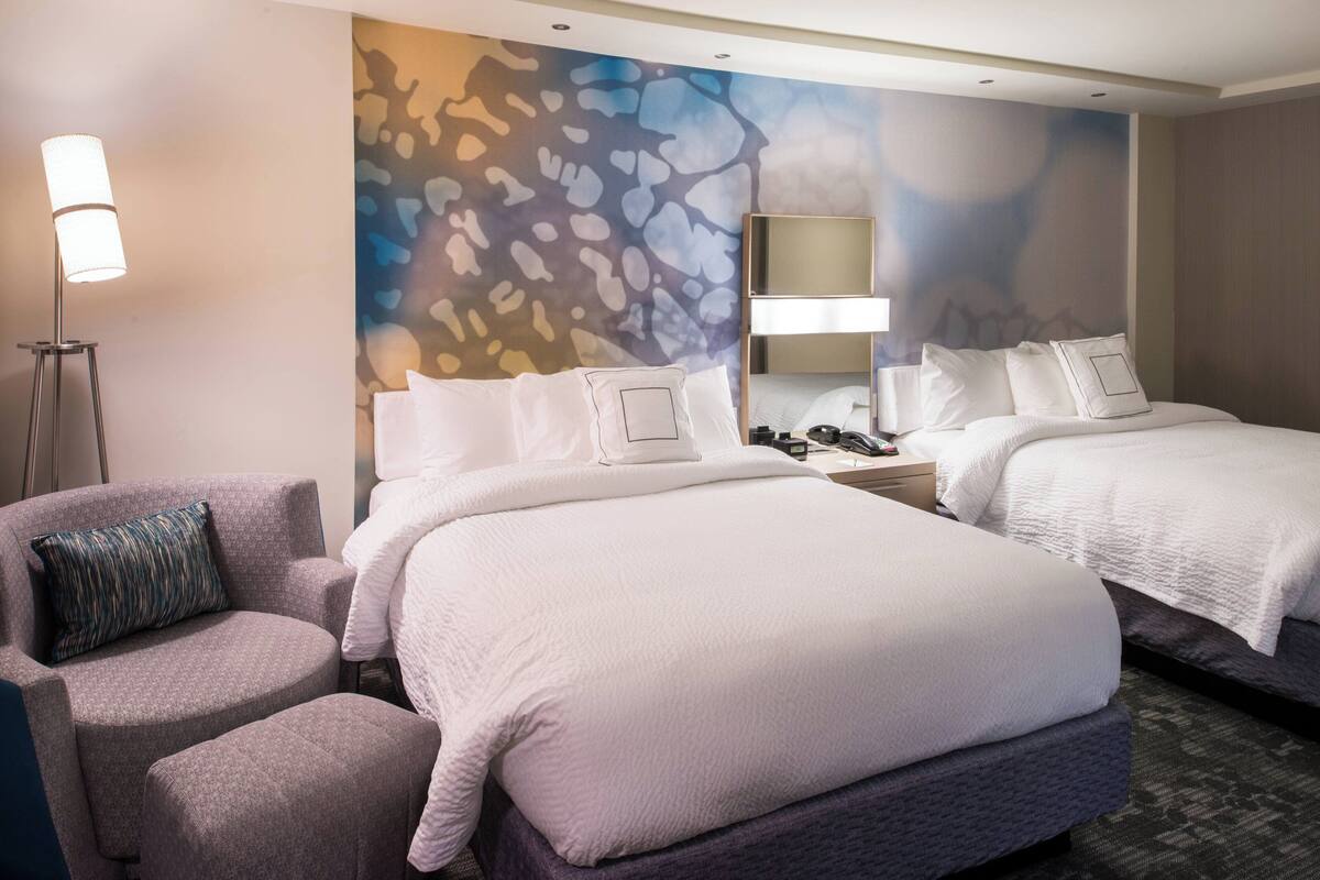 Une chambre d’hôtel avec deux lits, un coin salon, une lampe et un mur au décor texturé.