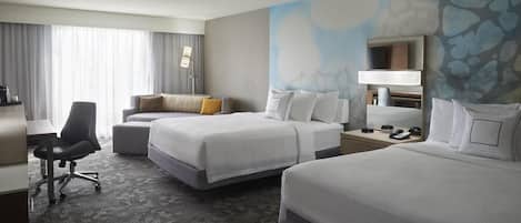 A hotel room with two beds, a desk, a chair, and a large window with curtains.