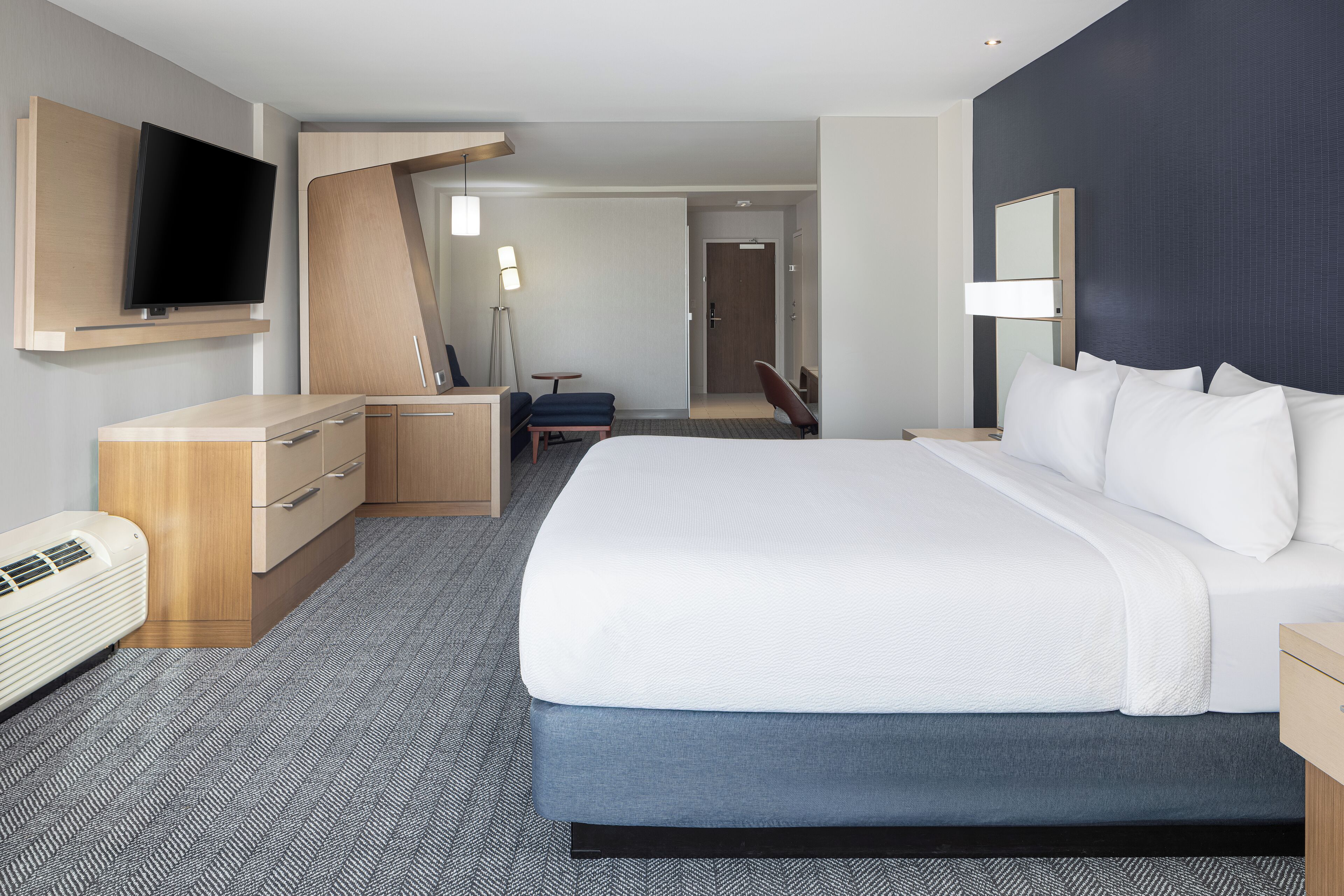 Une chambre d’hôtel avec un grand lit, un bureau, une chaise, une télévision et un miroir.