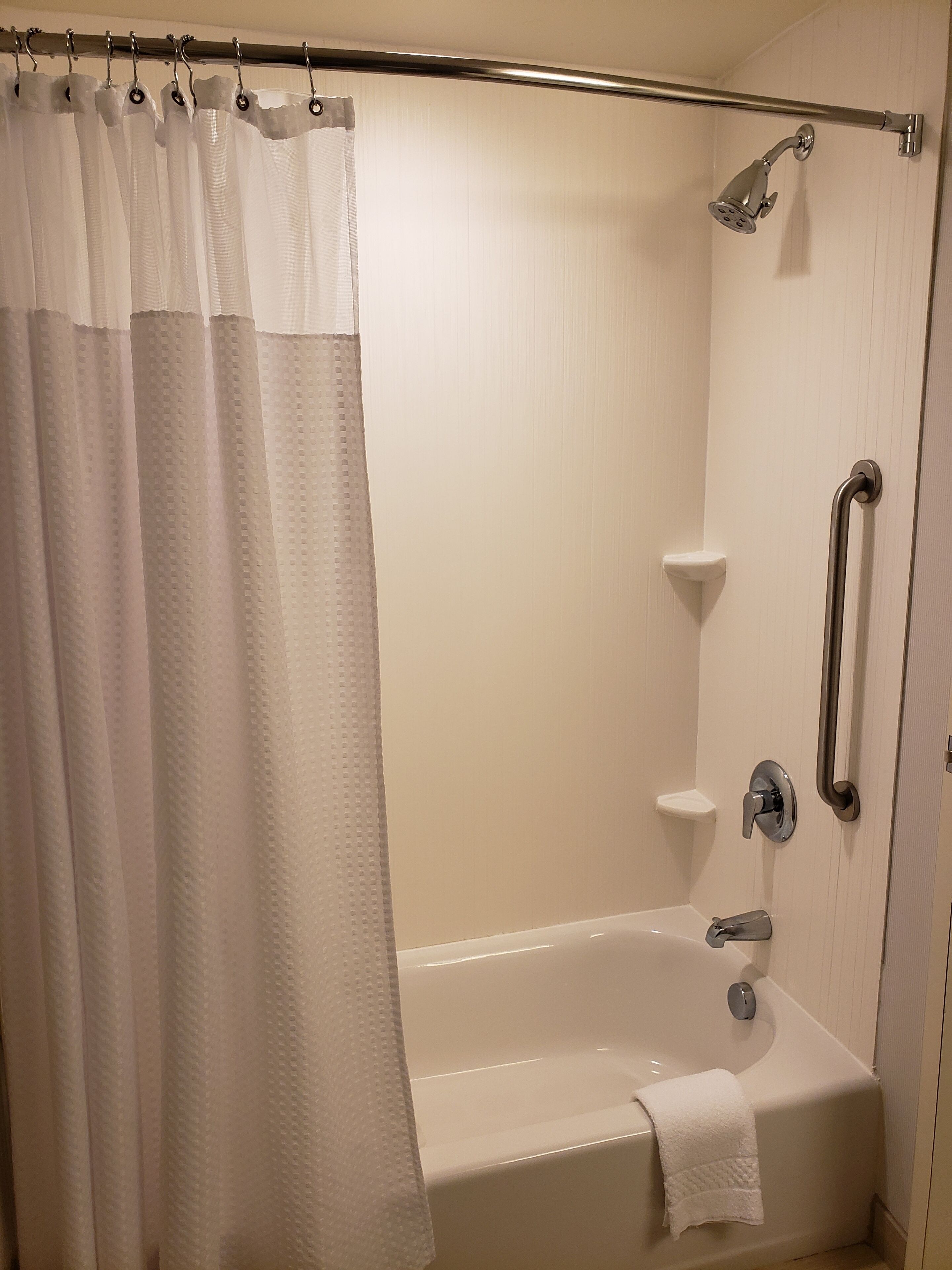 A bathroom with a bathtub, a shower, and a handrail.