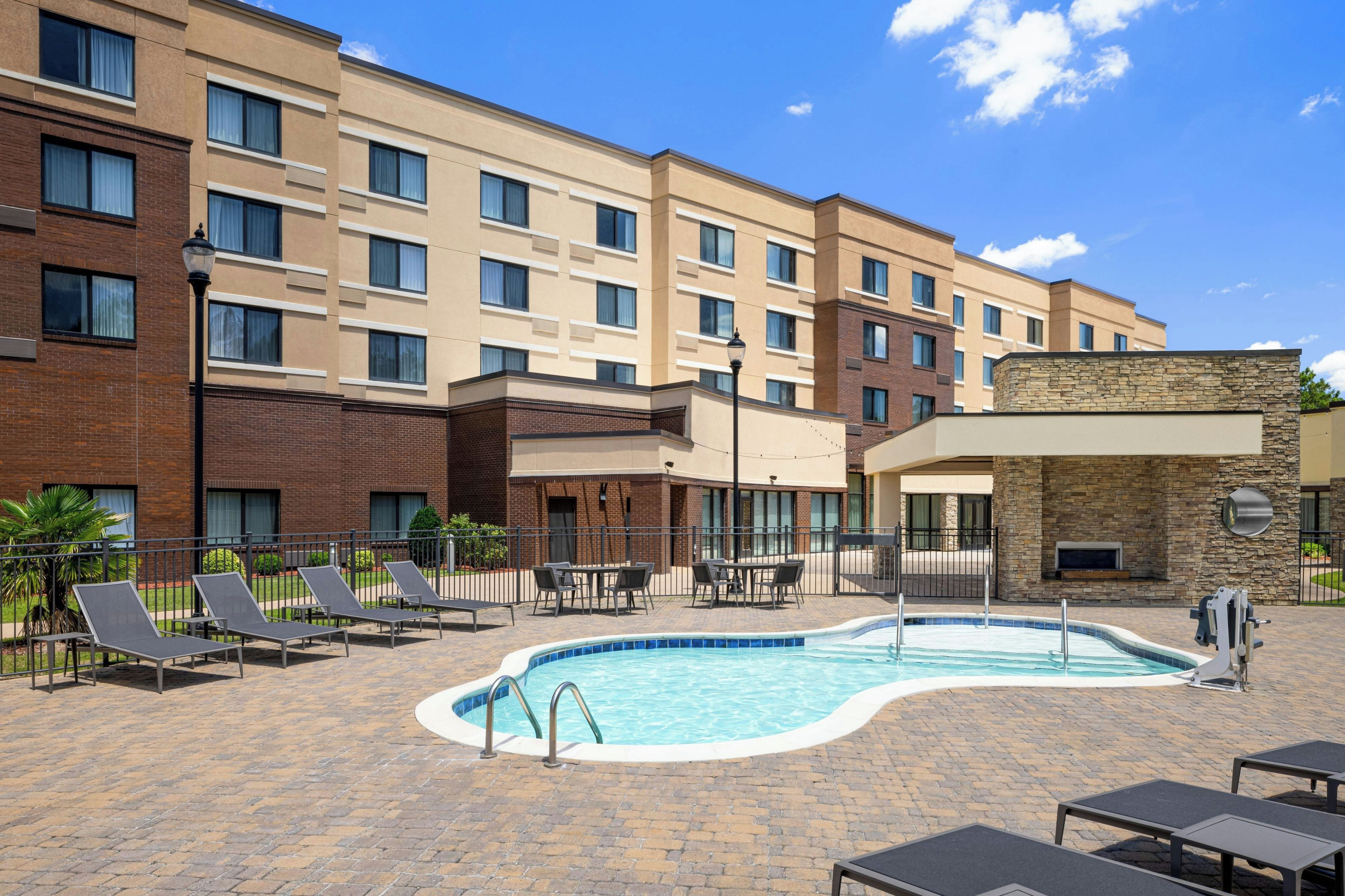 A hotel with a swimming pool, outdoor seating, and a brick facade.