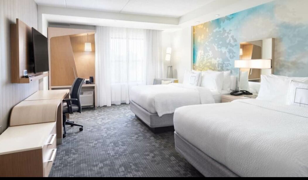 Une chambre d’hôtel avec deux lits, un bureau, une chaise, une télévision et un tableau au mur.