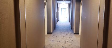 Pasillo de hotel con alfombra estampada, paredes color beige y una lámpara en el techo.