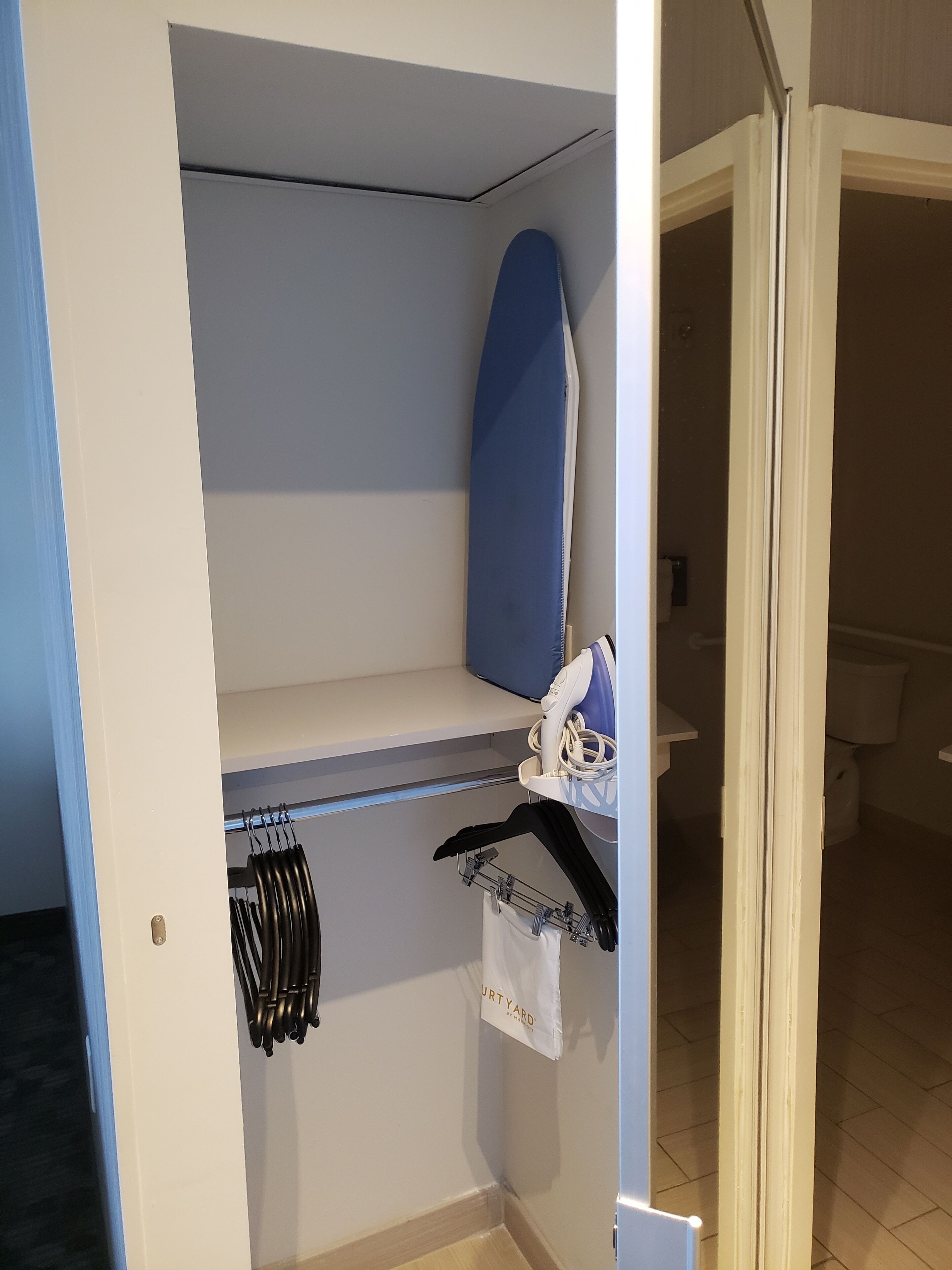 Una habitación con un armario blanco, una tabla de planchar azul y un perchero con perchas negras.