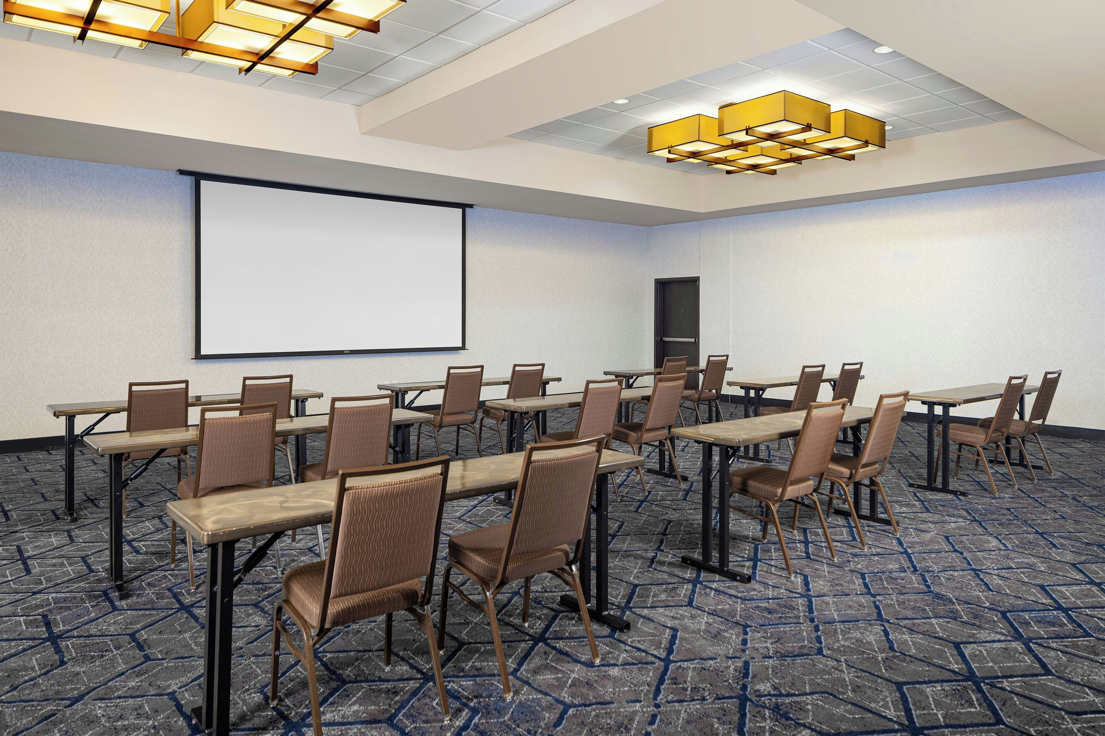Una sala de conferencias con una pantalla grande, varias mesas y sillas.