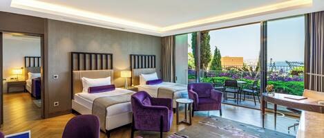 Habitación de hotel con dos camas, un comedor con mesa y sillas, y un balcón con vistas al mar.