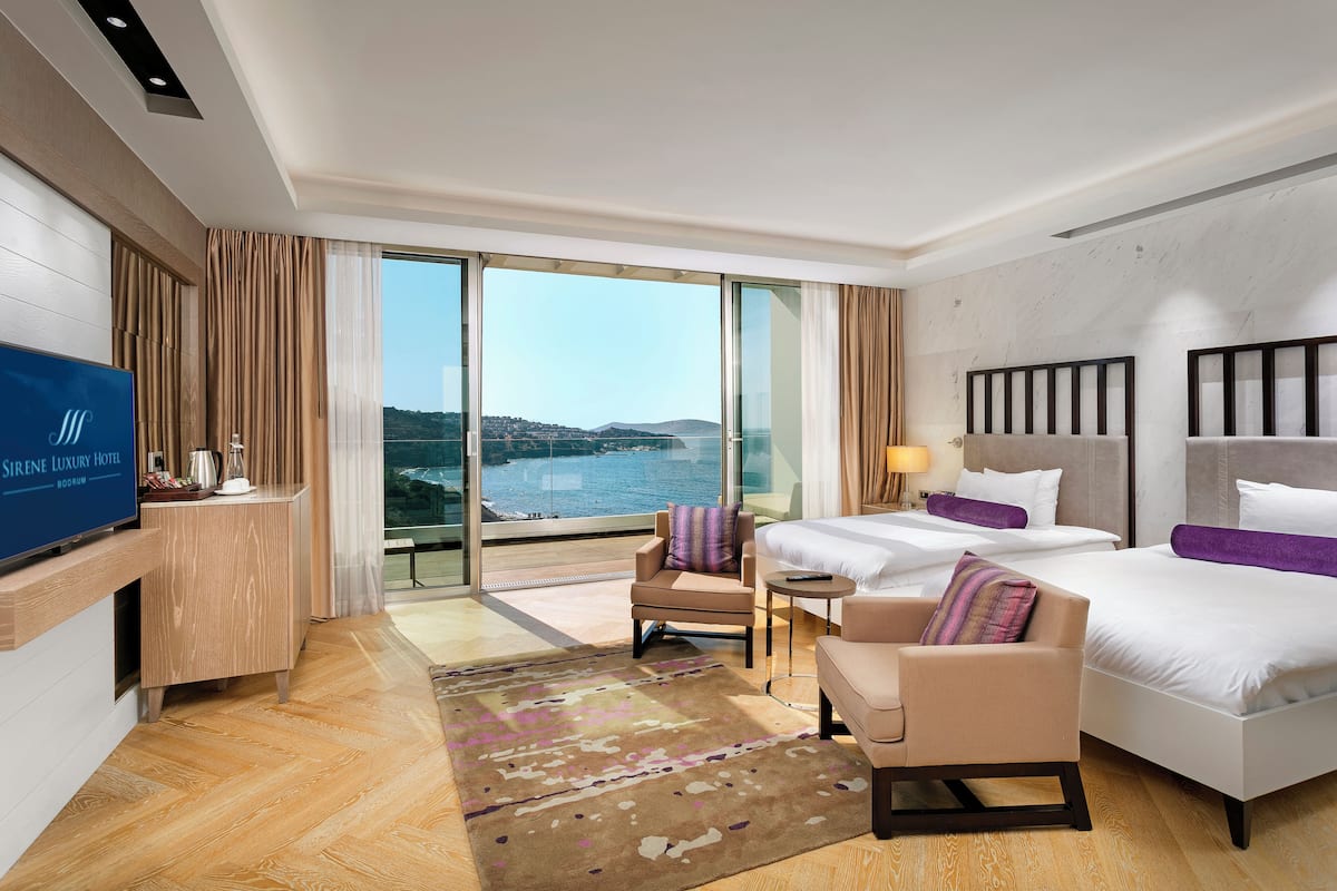 A hotel room with a large window, a bed, a chair, a desk, and a television.