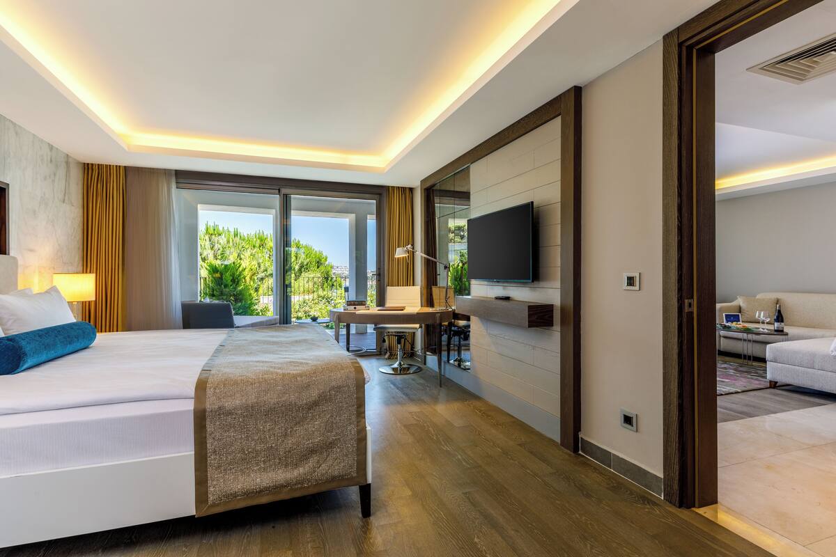 A modern hotel room with a large bed, a desk with a chair, a flat-screen TV, and a sofa.
