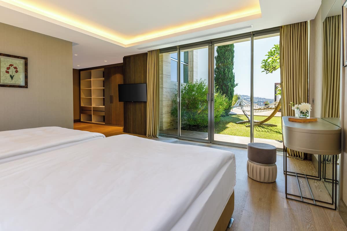 A hotel room with two beds, a TV, a small table, and a view of the outdoors.
