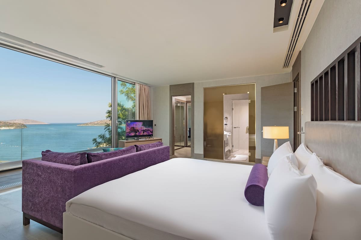 A hotel room with a large bed, a sofa, a TV, and a view of the sea.
