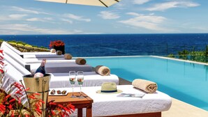 Un área de descanso junto a la piscina con vista al océano, una botella de champán, dos copas y una bandeja con aperitivos.