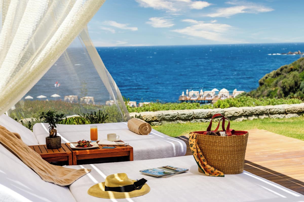 A cozy outdoor seating area with a view of the ocean, a wicker basket, a hat, and a small table with a plant and a drink.